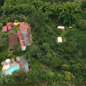 An aerial view of a residential area with multiple houses, a swimming pool, and dense surrounding vegetation. - Finca Turistica Machangara (Quimbaya)