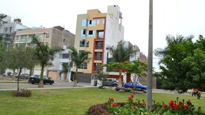 Un immeuble résidentiel à plusieurs étages, doté d’une architecture moderne, entouré de pelouses bien entretenues et de palmiers.