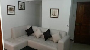 Un salon avec un canapé d’angle beige, deux coussins noirs et trois tableaux encadrés accrochés aux murs.