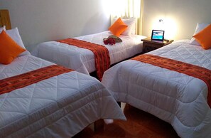 A hotel room with three single beds, each with white bedding and orange accents. There is a laptop on a bedside table, and a small table with a lamp and a flower. - Lodge Viñas del  Sol (Grocio Prado)