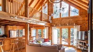 A spacious cabin with a loft bedroom, a dining area, and a living room with a large window overlooking the outdoors. - Whitewater Mountain Cabin on the Cullasaja River  (Highlands)