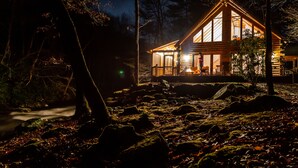 A log cabin with a large front porch, surrounded by a forested area. - Whitewater Mountain Cabin on the Cullasaja River  (Highlands)