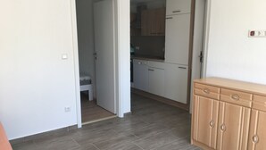 A kitchen with white cabinets, a wooden countertop, and a built-in oven. There is a door leading to a bedroom with a bed and a nightstand. - Monteurzimmer Leimen (Leimen)