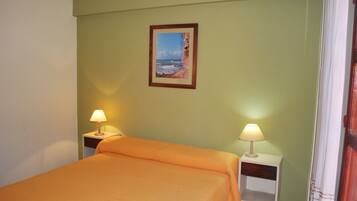 A room with a bed, two bedside tables with lamps, a framed picture on the wall, and a window with curtains.