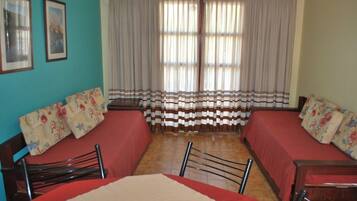 A room with two beds, a dining table, chairs, and curtains.