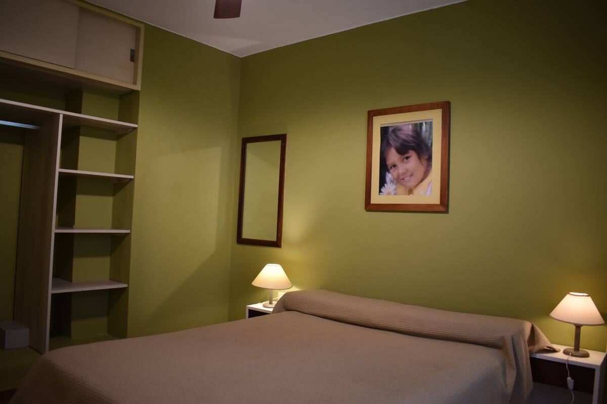 Une chambre à coucher avec un lit, deux lampes de chevet, une armoire et un tableau encadré au mur.