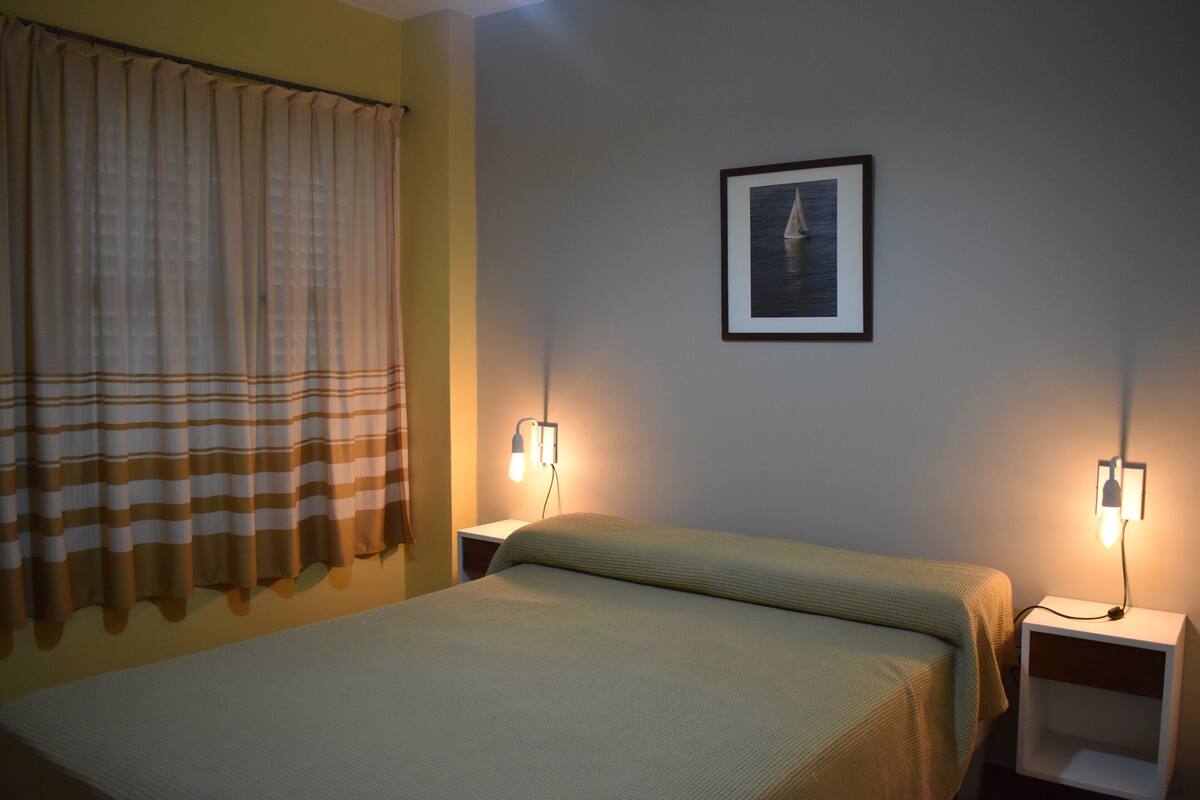 Une chambre avec un lit, deux tables de chevet, un tableau encadré au mur et des rideaux.