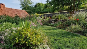 A garden with a stone wall, various plants, and a red-tiled roof structure.
