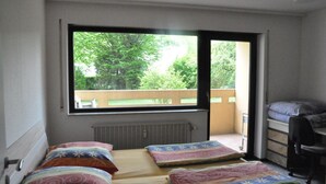 Una camera del dormitorio con due letti, una scrivania e una finestra che dà su un balcone con alberi.