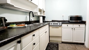 A compact kitchen with white cabinets, a black countertop, a microwave, and a stove. - Two bedrooms Home Duplex in Historic Downtown lakeland (Lakeland)