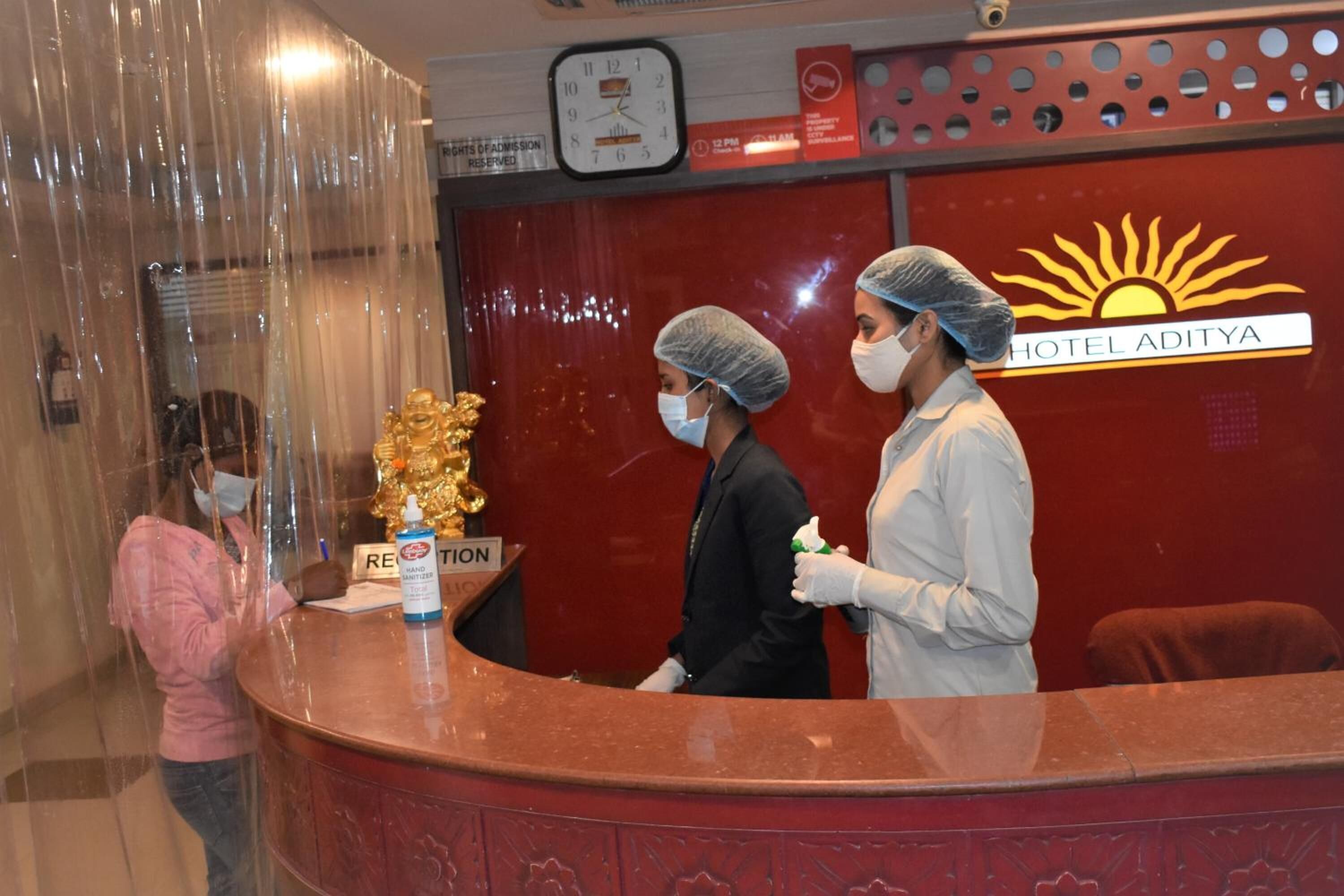 A hotel reception desk with a clock, a sign for room reservation, and a logo for Hotel Aditya.