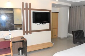 Habitación de hotel con una televisión de pantalla plana en la pared, un escritorio de madera con una silla, un cesto de basura pequeño y una cama.