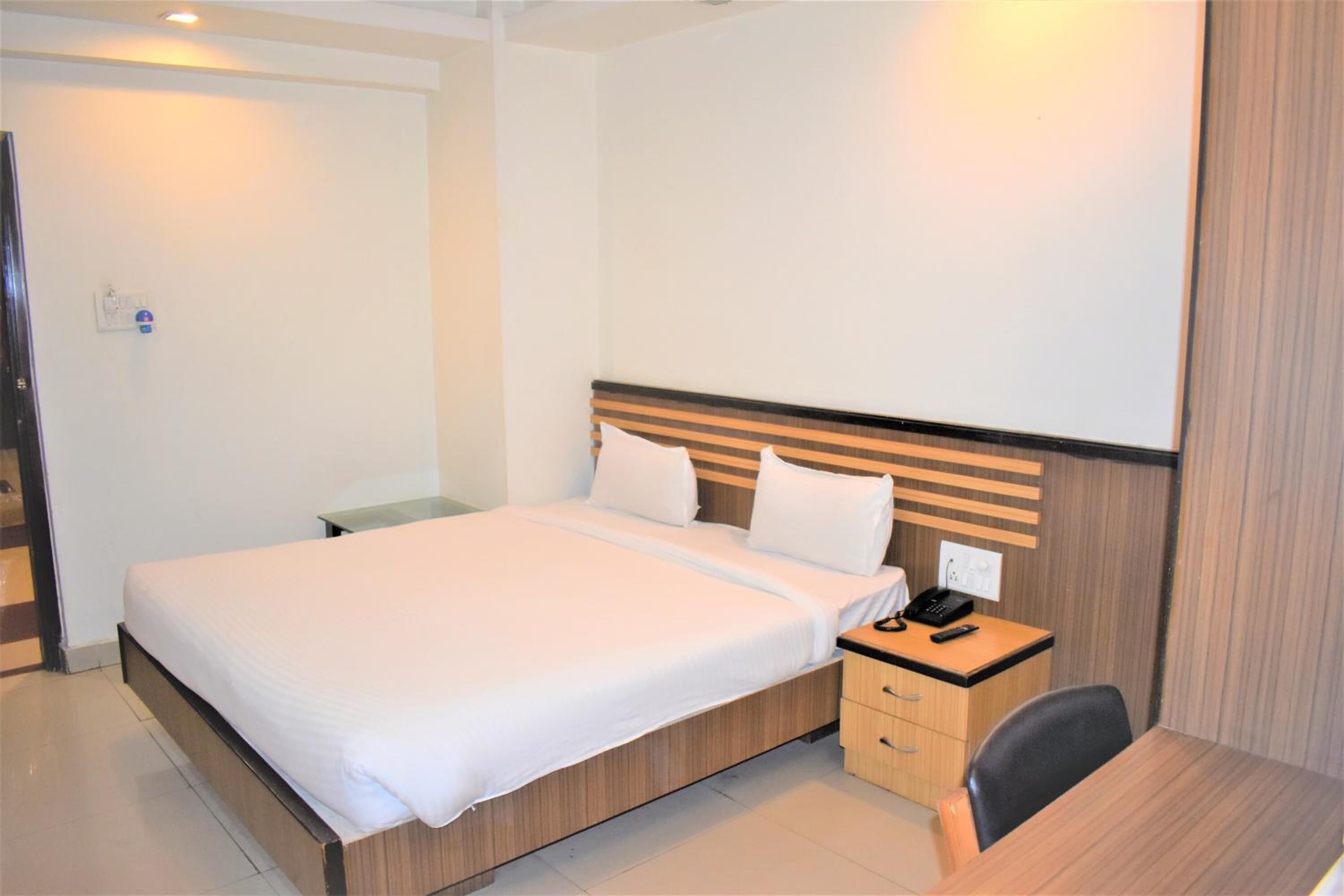 Une chambre d’hôtel avec un grand lit, une table de chevet avec un téléphone et un petit bureau avec une chaise.
