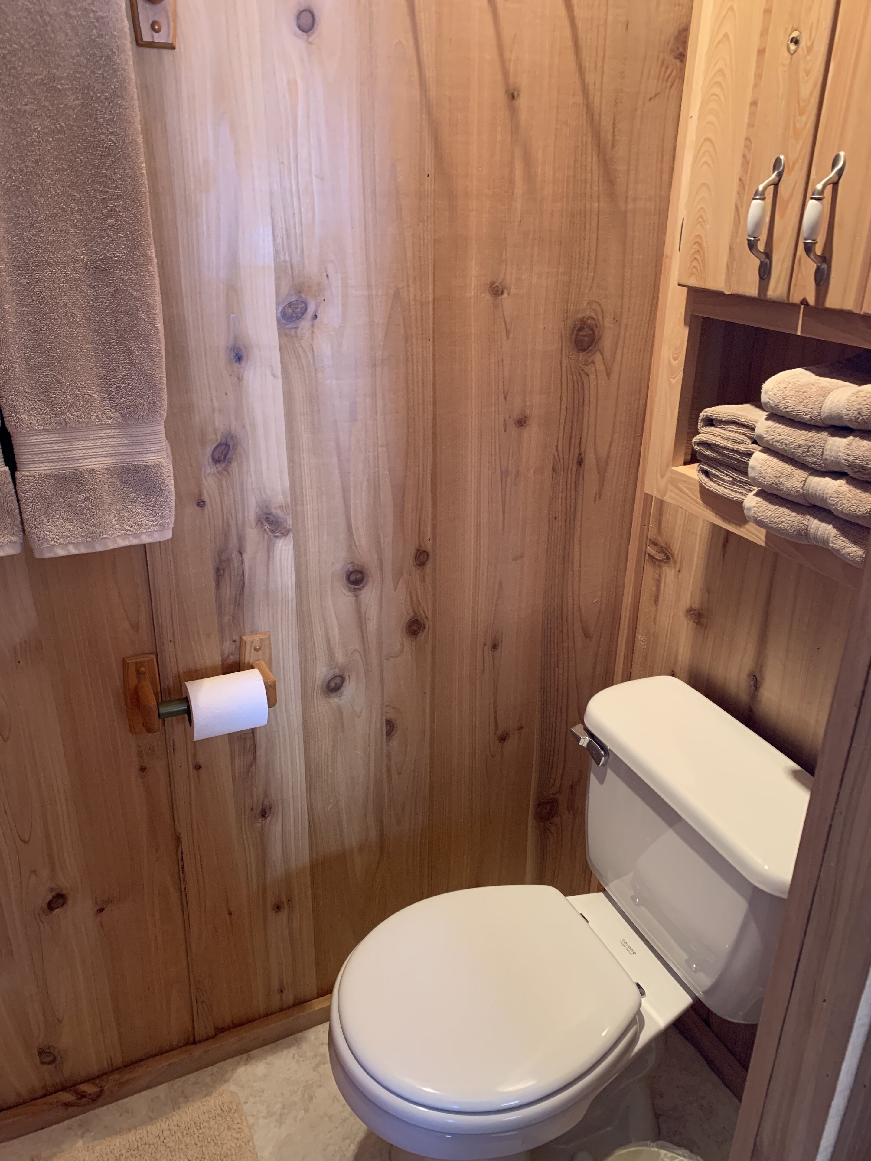 Et badeværelse i træ med toilet, håndklædestige og toiletpapirholder.