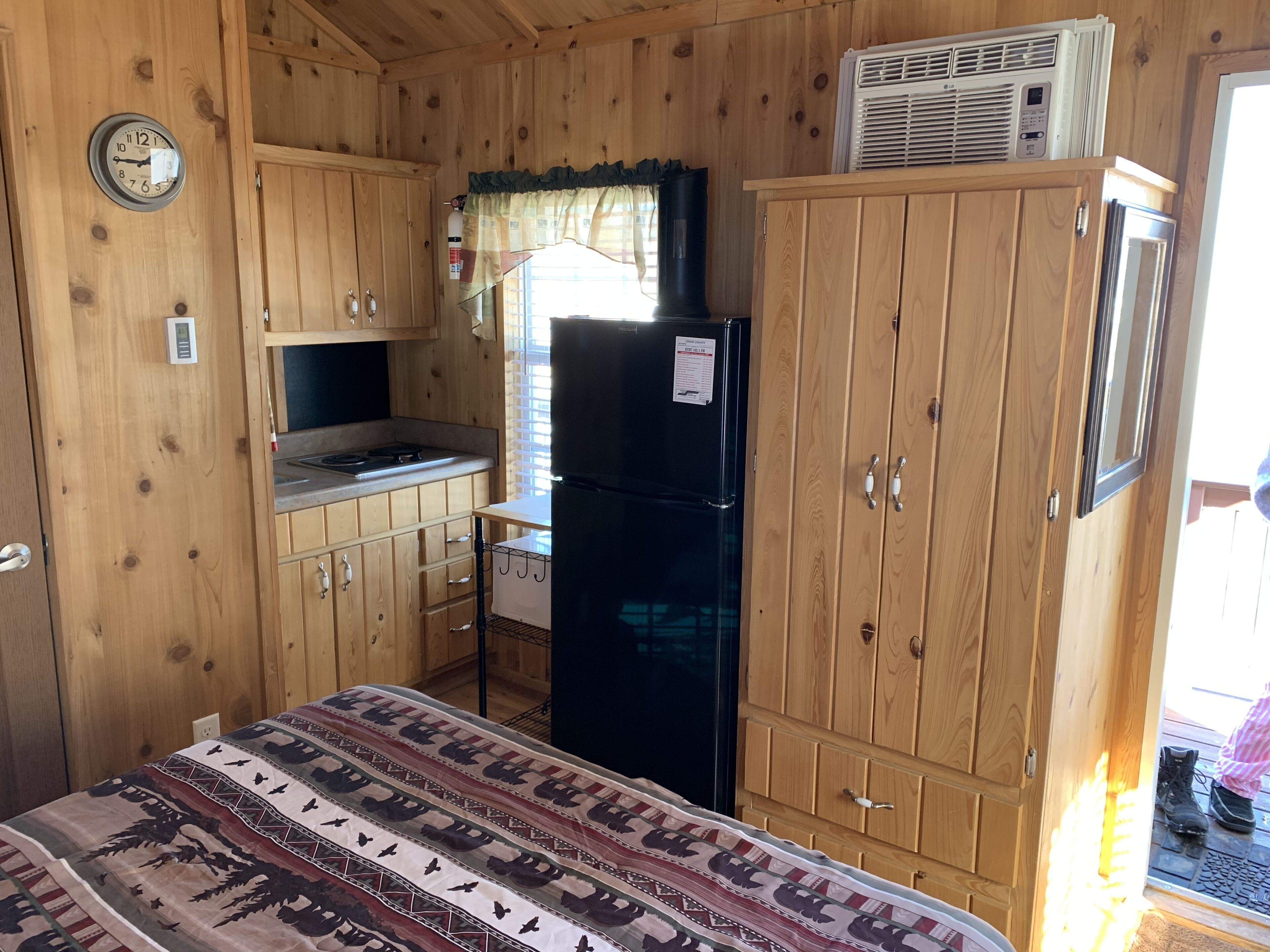 A compact wooden cabin with a kitchenette, including a stove, refrigerator, and cabinets.
