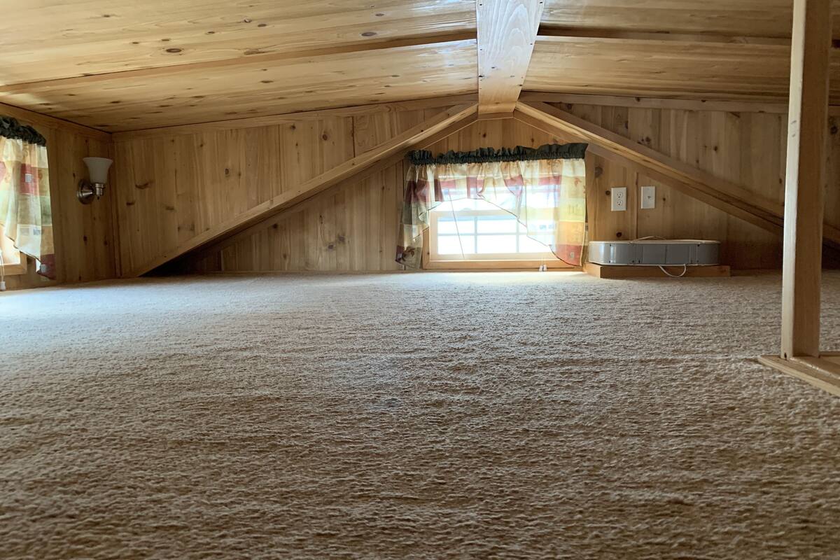 A spacious attic room with a sloped ceiling, carpeted floor, and a large window with curtains.