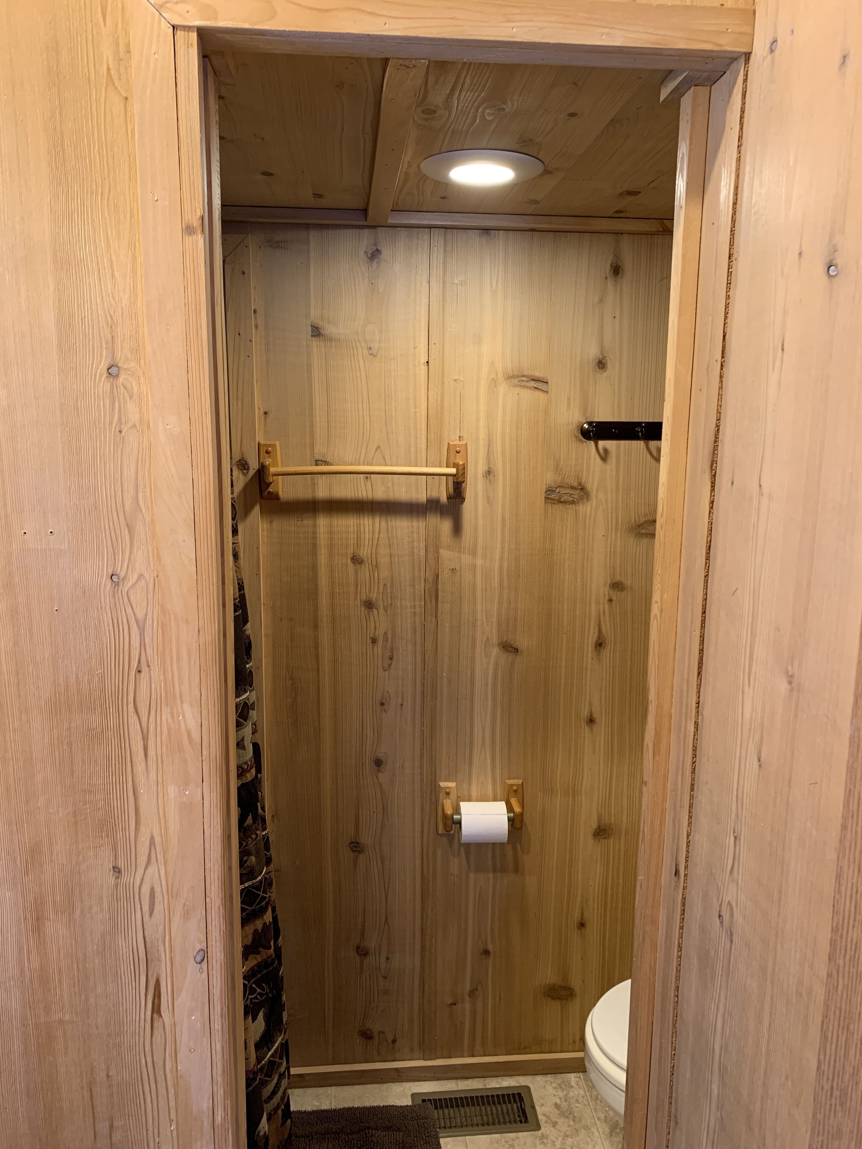 Ein Badezimmer aus Holz mit Toilette, Handtuchhalter und Duschvorhang.