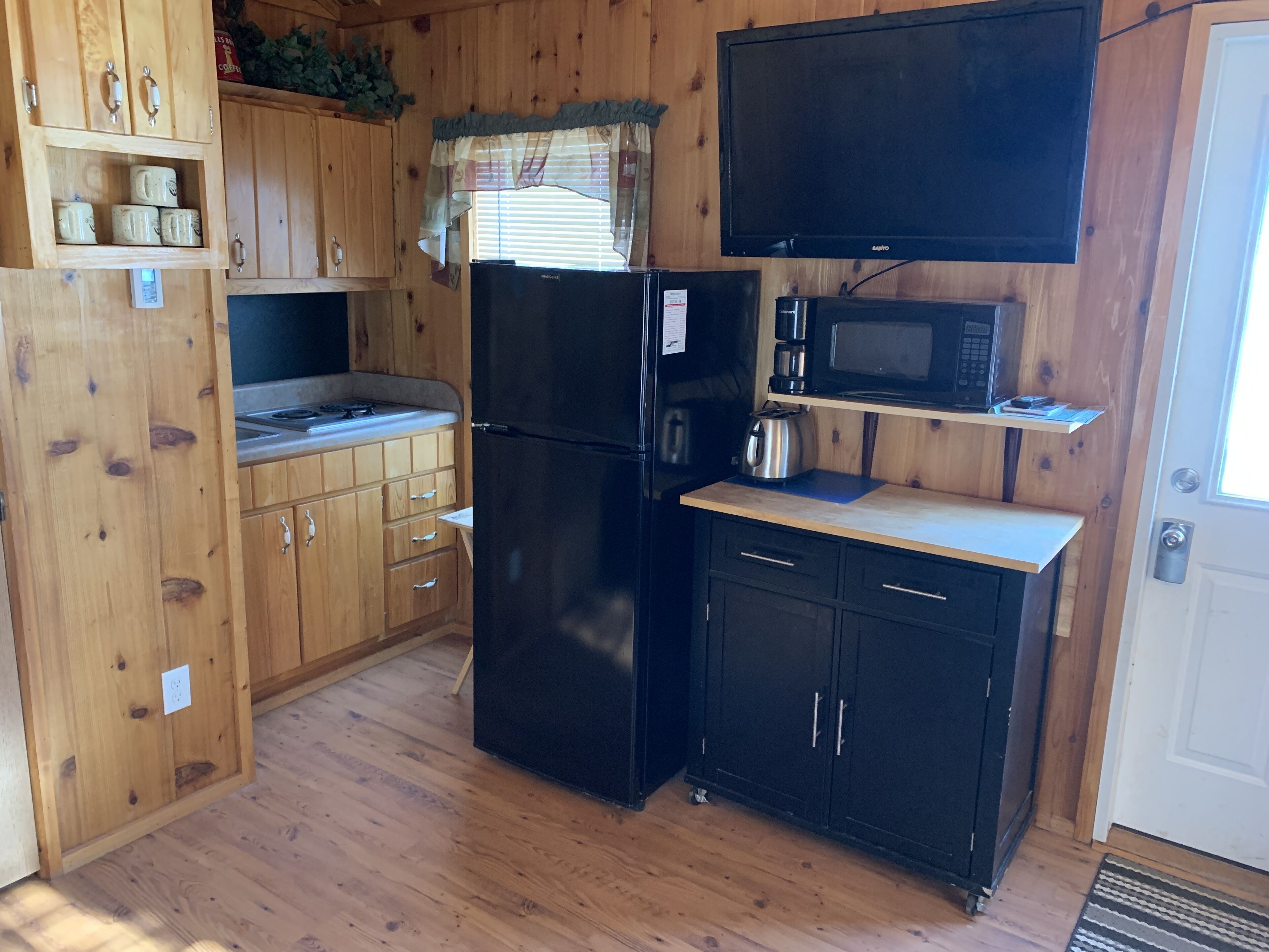 A compact kitchen with wooden cabinets, a black refrigerator, a microwave, and a coffee maker.