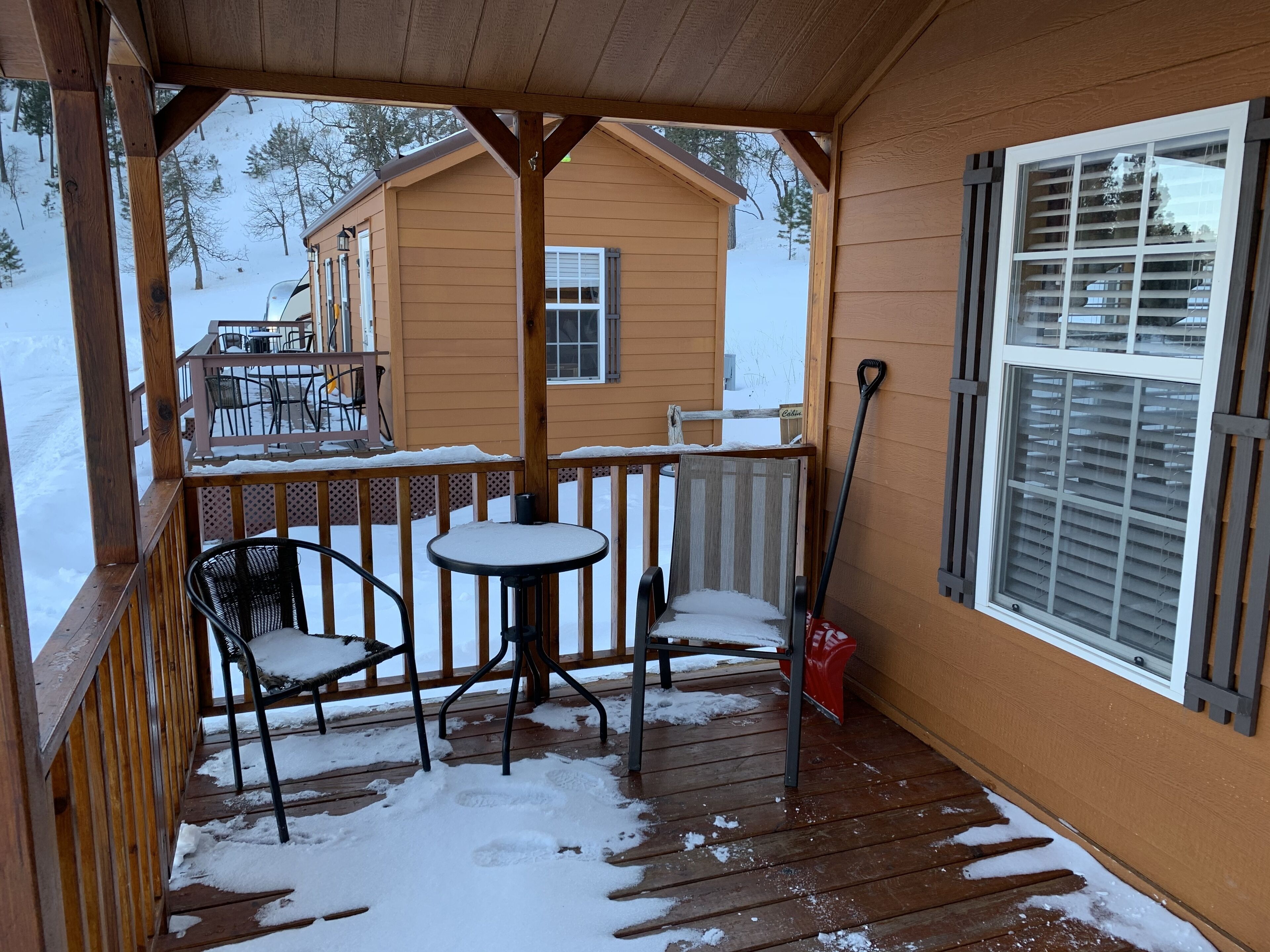 Eine Holzdielen-Terrasse mit Tisch und Stühlen, bedeckter Boden mit Schnee und ein Gebäude im Hintergrund.