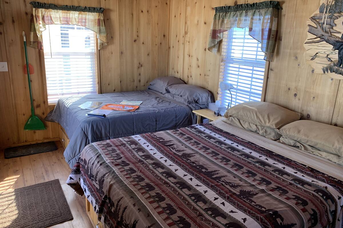 A wooden room with two beds, a desk, and a window with curtains.