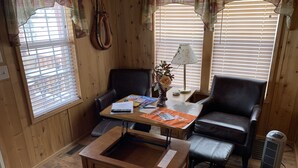 Ein gemütliches Zimmer mit Holzwänden, einem Ledersofa, einem Couchtisch und einem Schreibtisch mit Papier und Büchern.