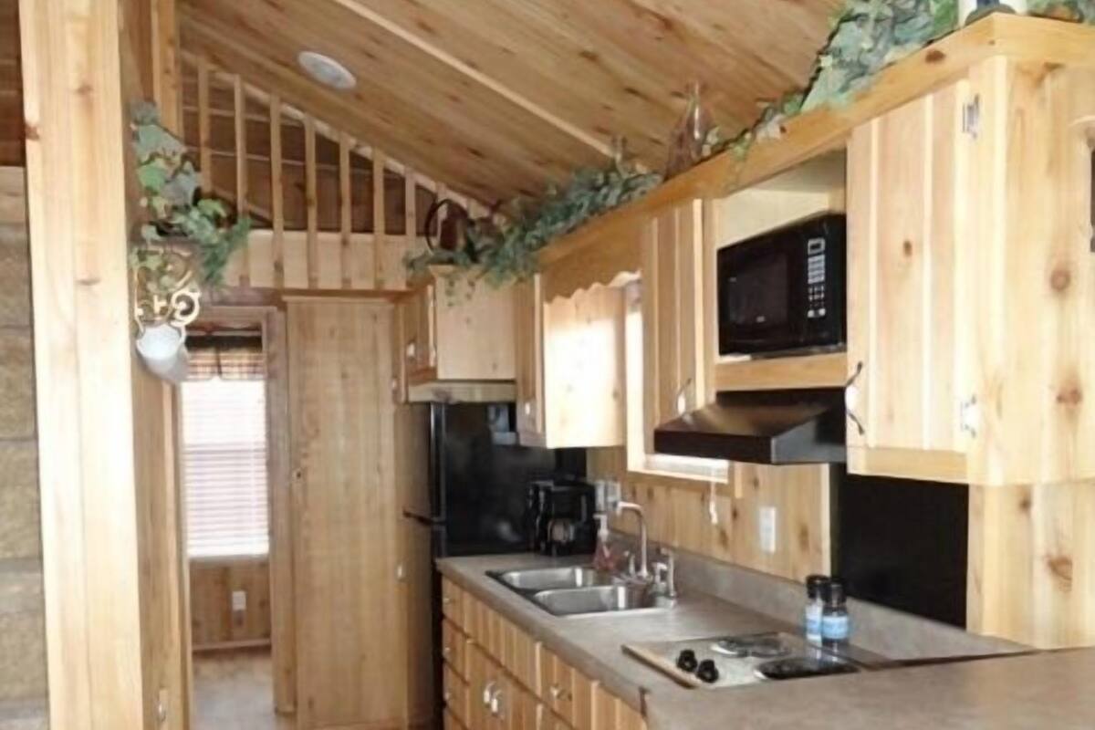 A wooden kitchen with a central island, built-in appliances, and a view into the adjacent room.