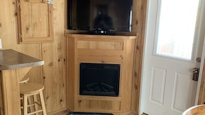 Ein Holzblockhaus-Innenraum mit einem Fernseher über einem Kamin, einer Tür und einem kleinen Hocker.