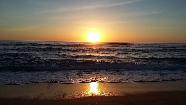 A sunset over the ocean with waves on a beach.