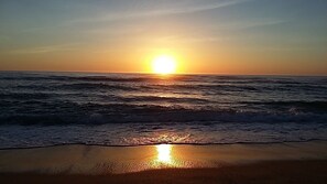 A sunset over the ocean with waves on a beach.