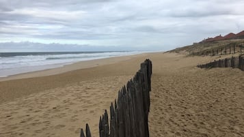 Ein sandiger Strand mit einem Holzzaun im Vordergrund und einem bewölkten Himmel.