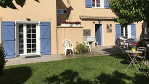 A two-story building with blue shutters, a small outdoor seating area, and a garden.