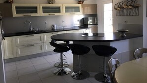 A modern kitchen with a central island, bar stools, and a microwave.
