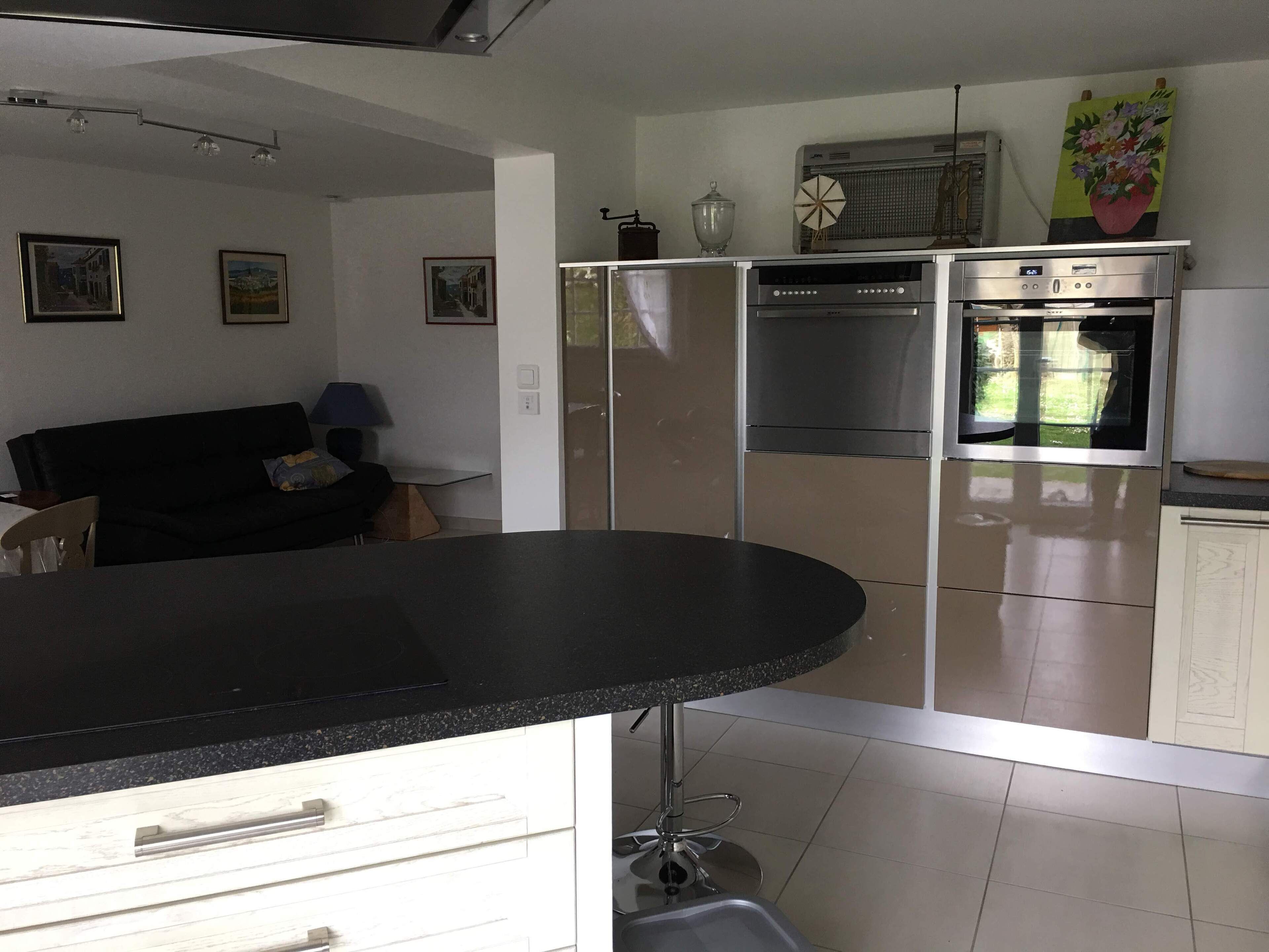A modern kitchen with stainless steel appliances, a black countertop, and a dining area with a chair.
