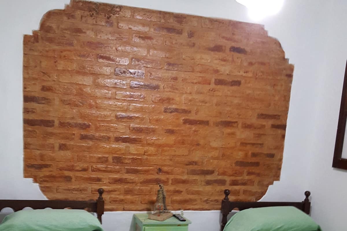 Ein Zimmer mit zwei Betten, einem grünen Nachttisch, einer Ziegelwand, einem Deckenventilator und einem gefliesten Boden.