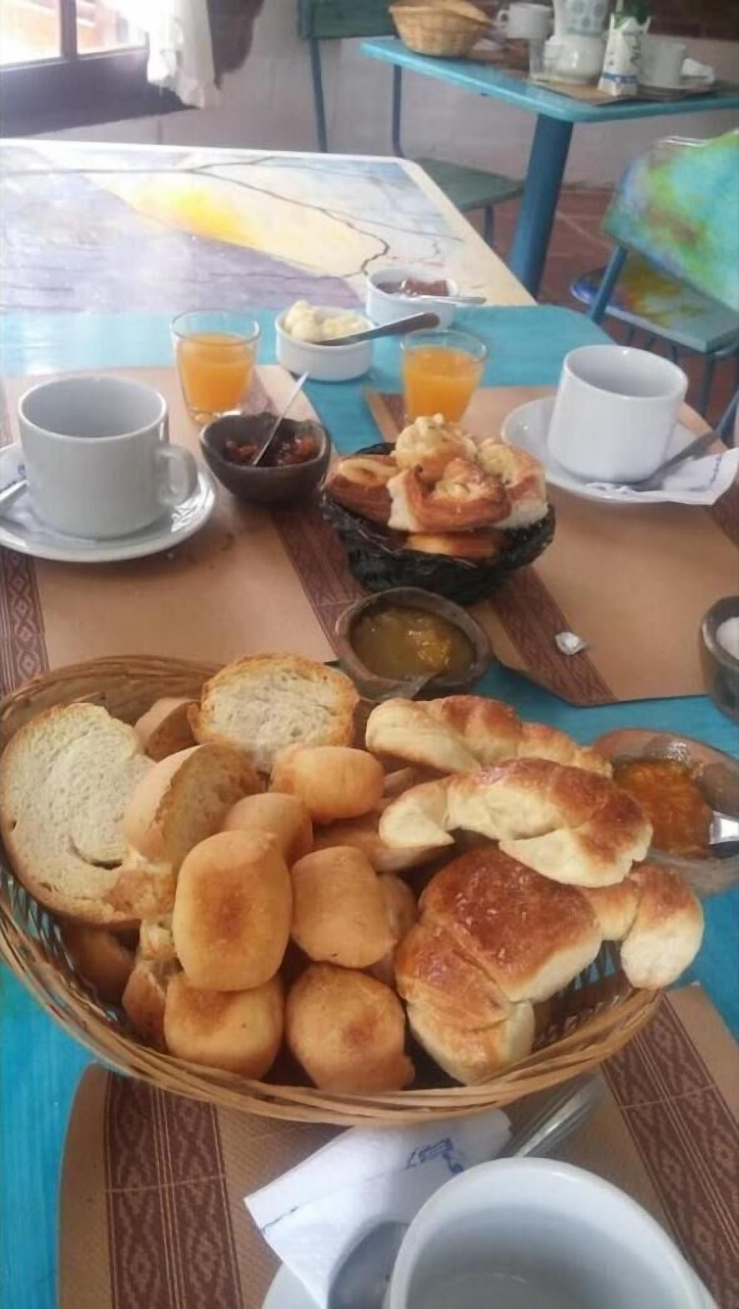 Una mesa de desayuno con panecillos, bollería y una cesta de pan.