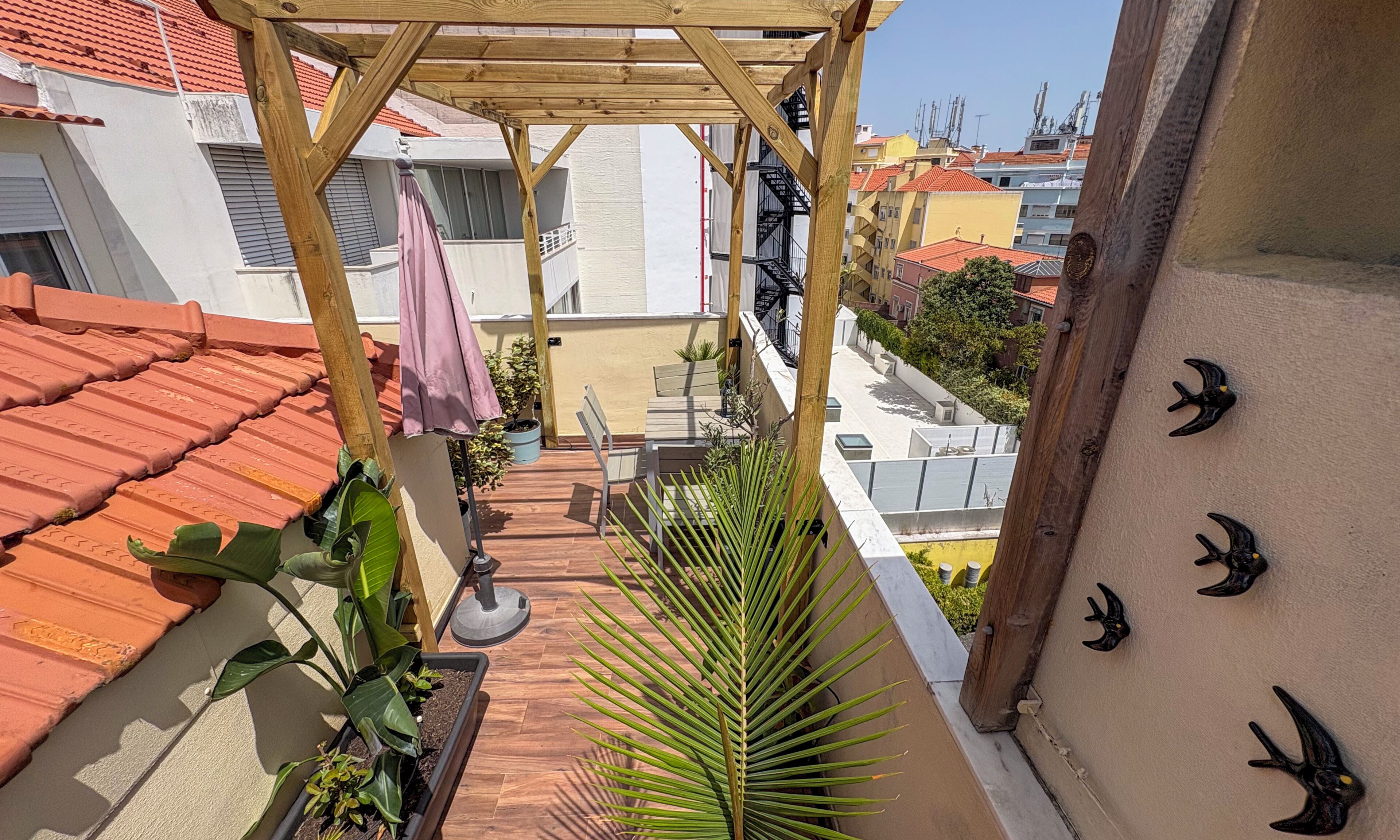 Un balcon agrémenté d’une pergola en bois, de plantes en pot et offrant une vue sur les bâtiments voisins.
