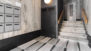 A modern lobby with a marble wall, a staircase, and a mail drop area.
