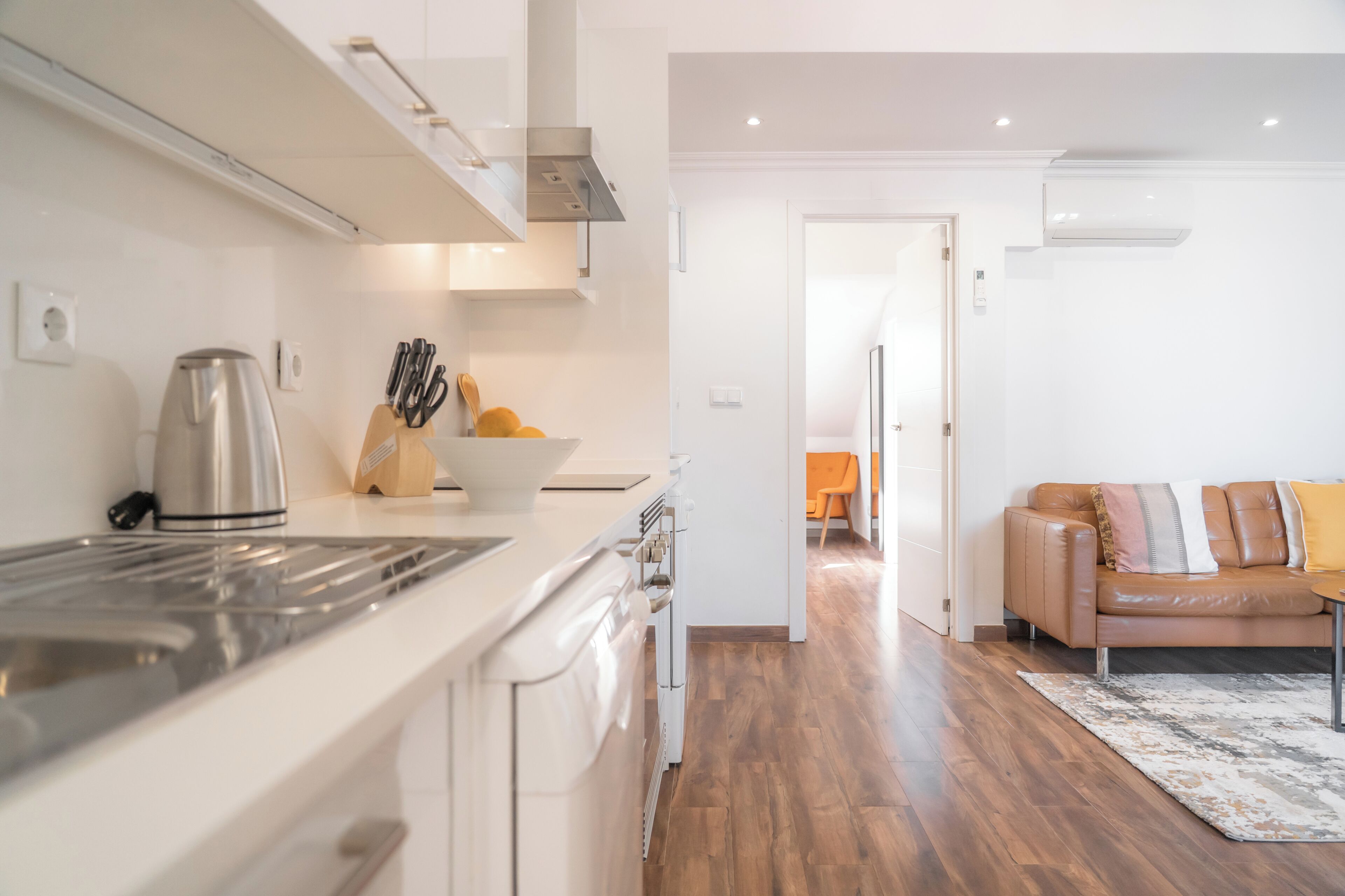 A modern kitchen with a stainless steel range hood, a kettle, and a bowl of fruit on the counter.