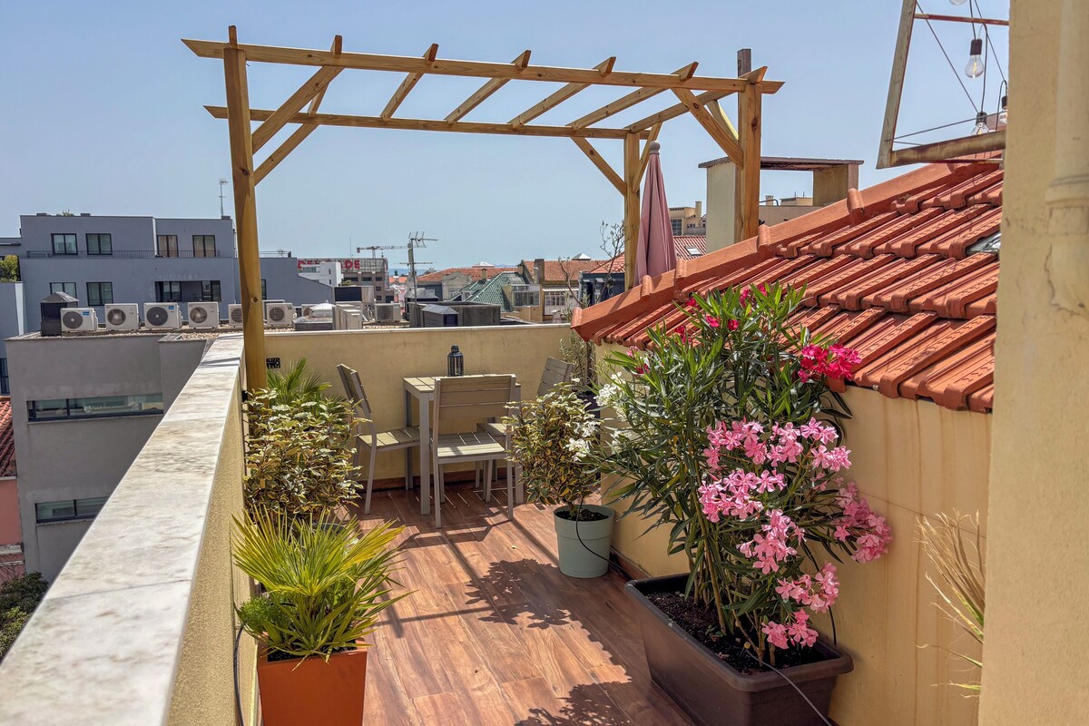 A rooftop terrace with a pergola, seating, potted plants, and a view of surrounding buildings.