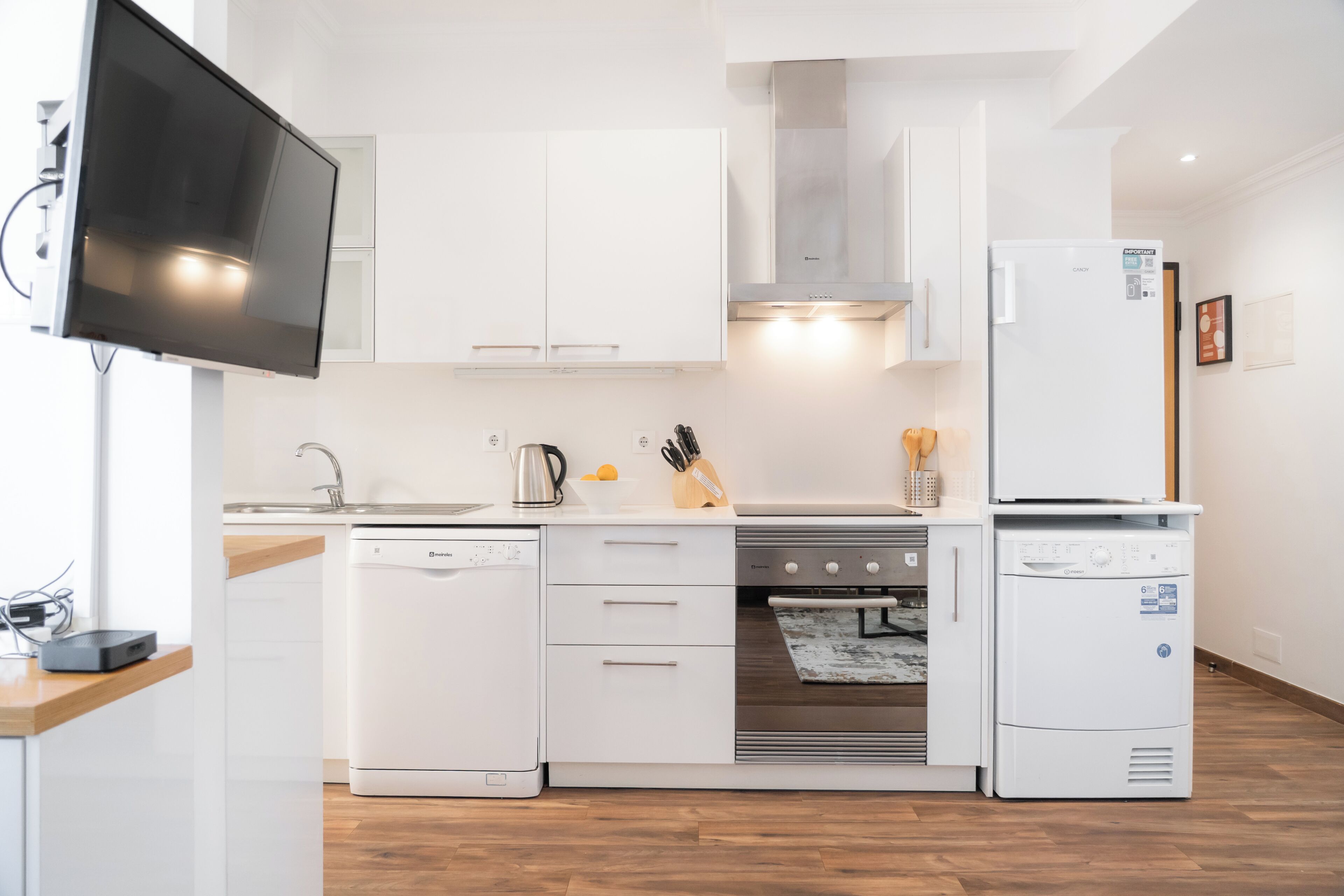 Una cocina moderna con armarios blancos, horno empotrado, lavavajillas y refrigerador.