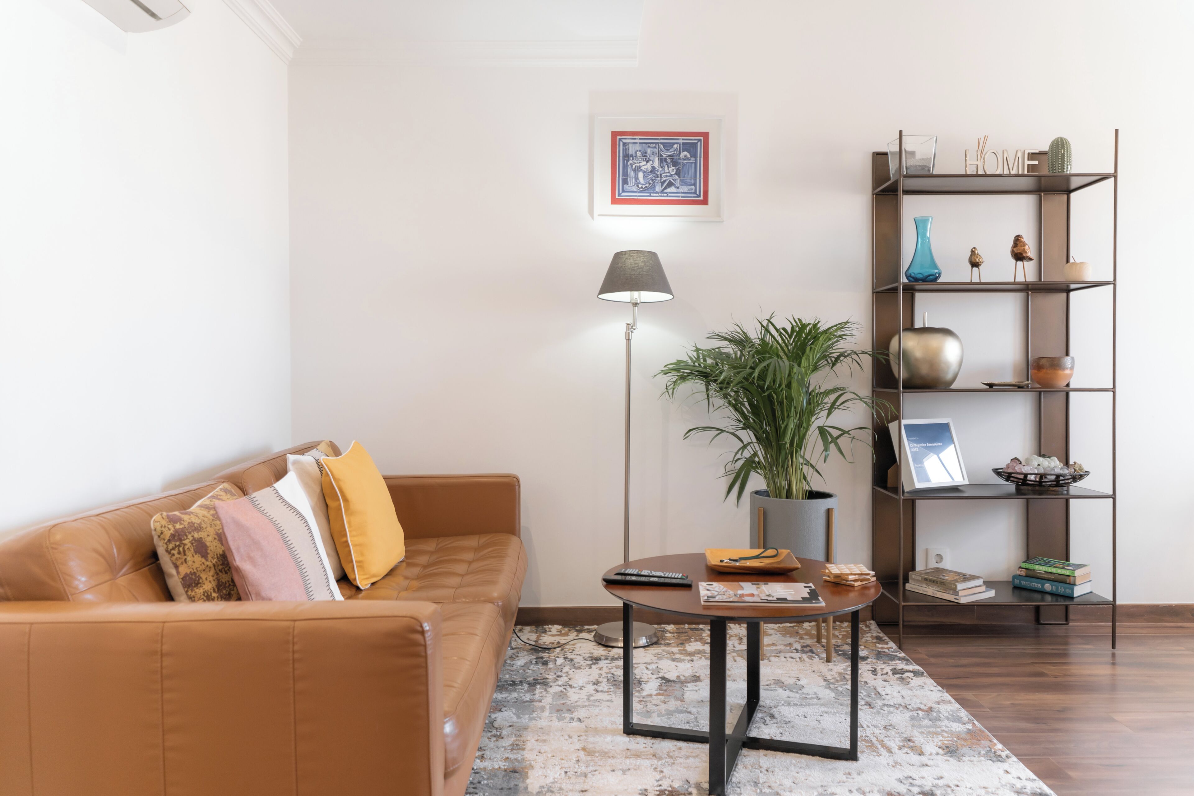 Un salon avec un canapé en cuir marron, une table basse ronde, un lampadaire, une plante en pot et une bibliothèque.