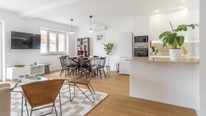 A modern kitchen with white cabinets, a dining area with a wooden table and chairs, and a large potted plant.
