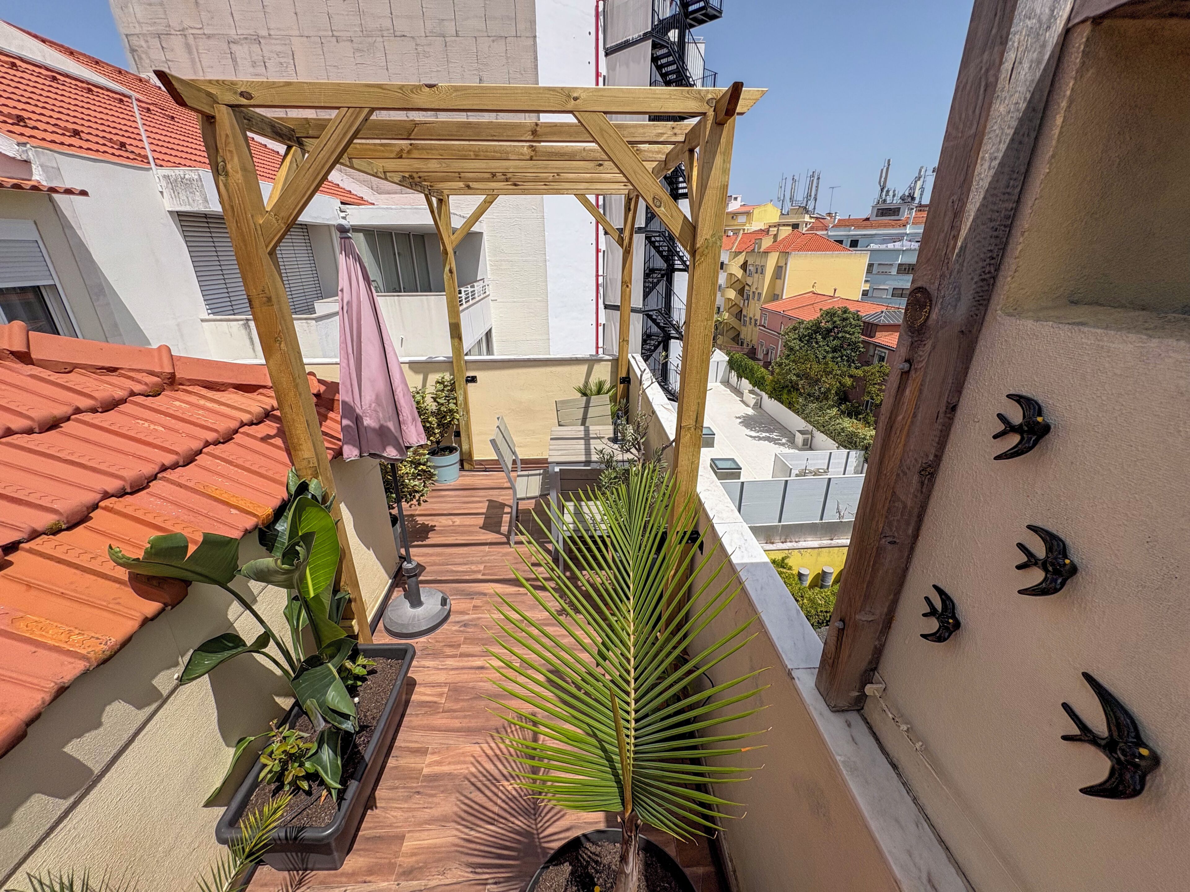 A rooftop terrace with a wooden pergola, potted plants, and a view of surrounding buildings.
