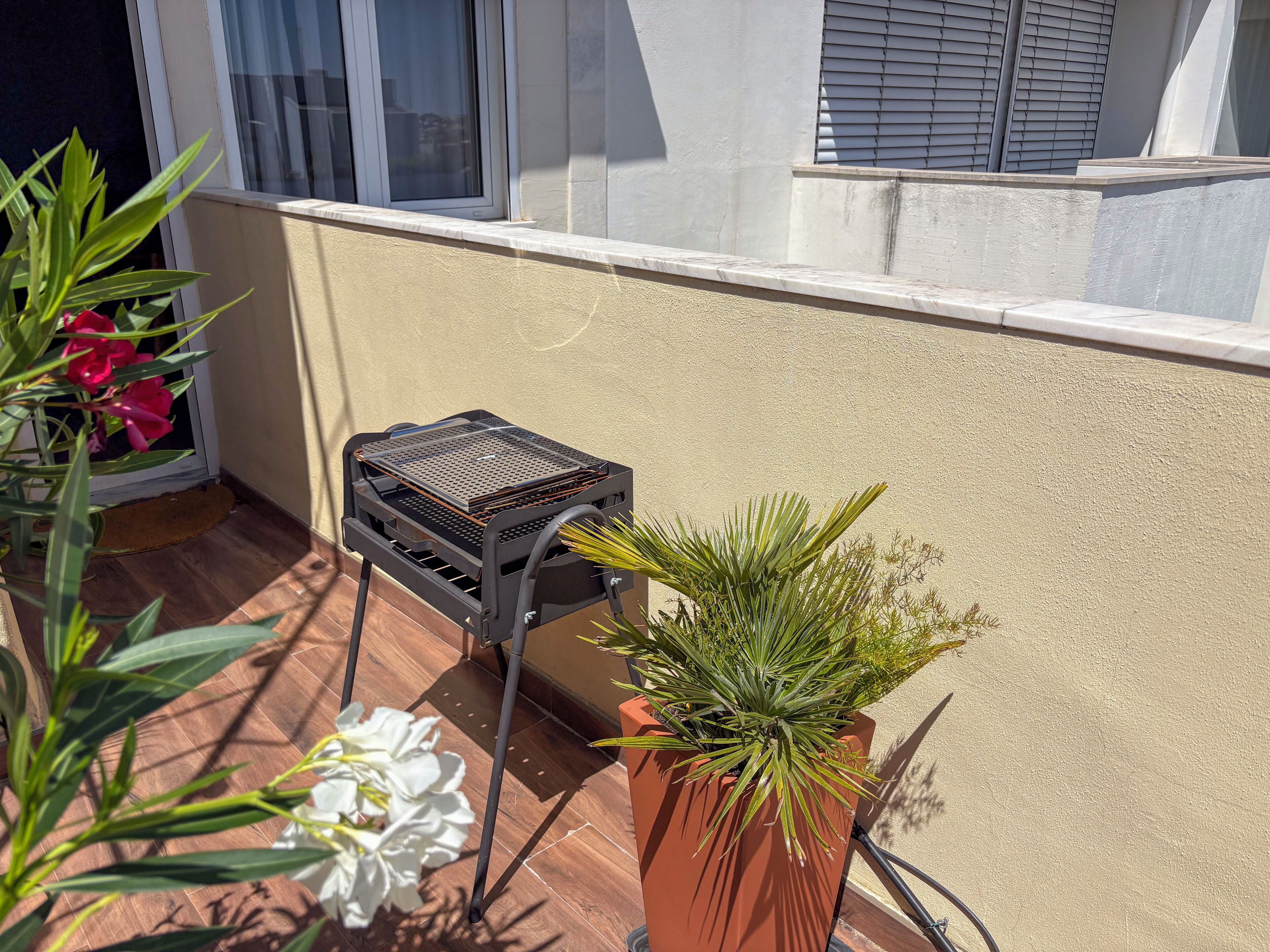A balcony with a barbecue grill, potted plants, and a window.