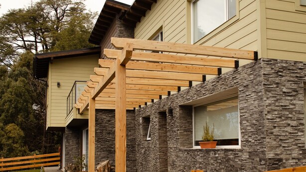 Een modern huis met een gevel van natuursteen, een houten terras en een stenen muur.