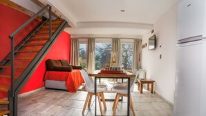 Een moderne woonkamer met een rode accentmuur, een houten trap, een bank, een eettafel met stoelen en uitzicht door grote ramen.