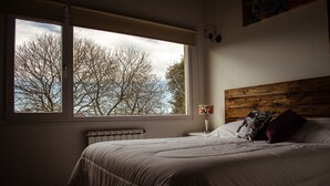 Een slaapkamer met een groot raam, een houten hoofdbord en een nachtkastje met een lamp.