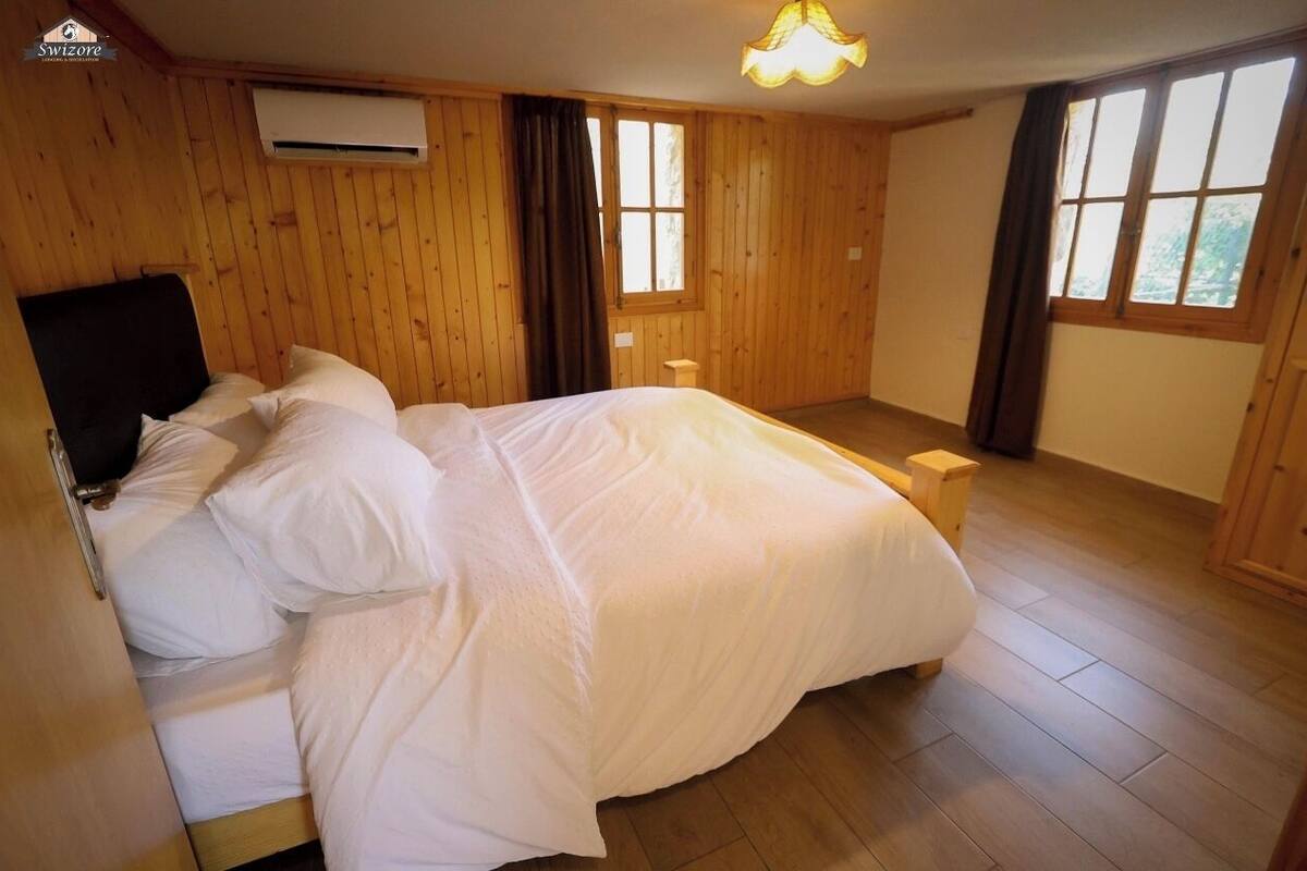 A wooden-paneled bedroom with a bed, a nightstand, and a window with curtains.