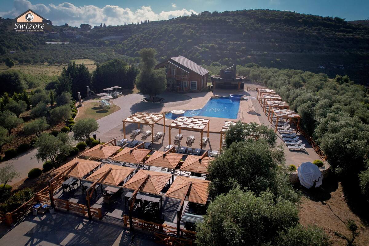 A resort with a swimming pool, outdoor seating, and a mountain backdrop.