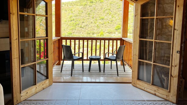 Een houten balkon met twee stoelen en een tafel, met uitzicht op een glooiend landschap.
